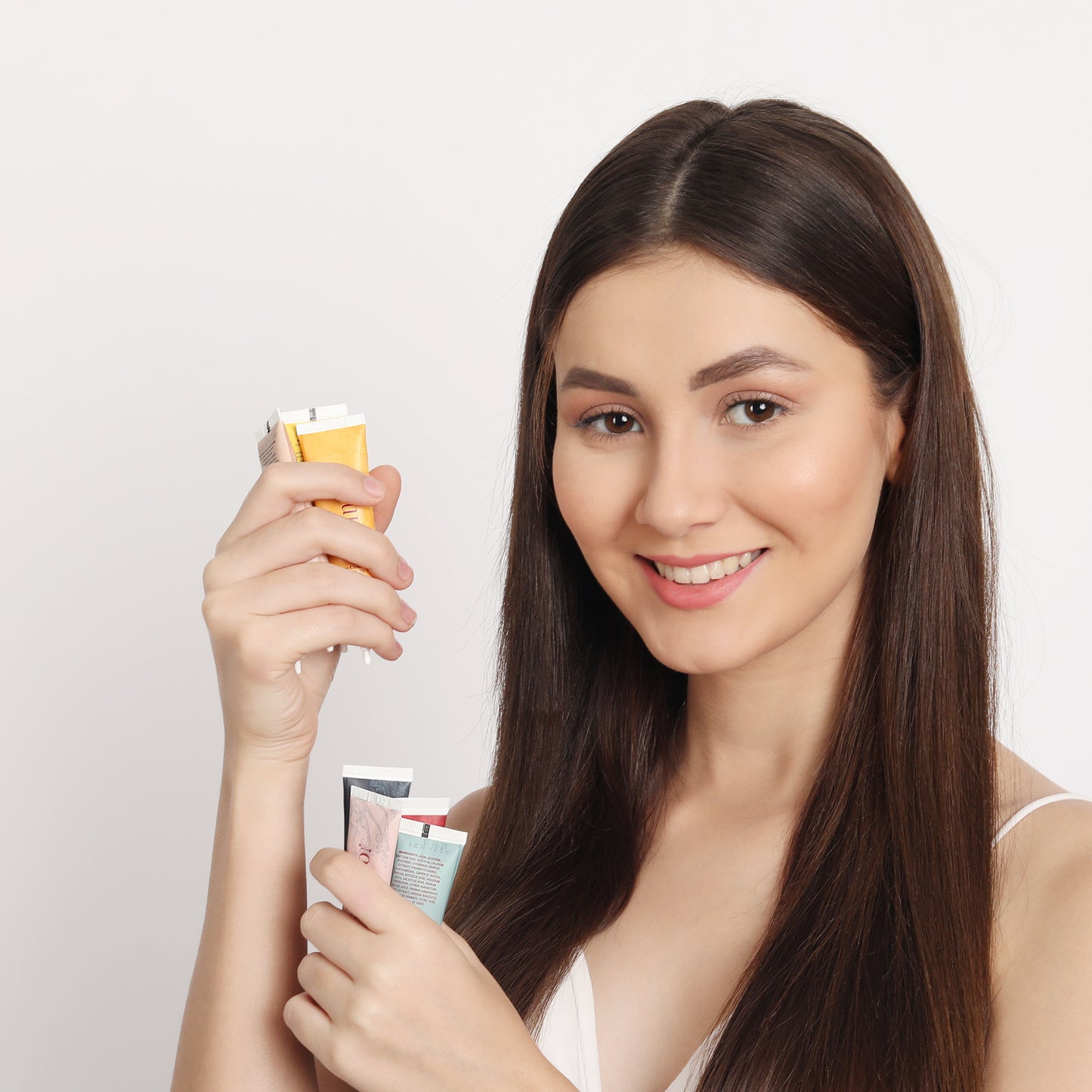 Woman holding skincare products against a plain background